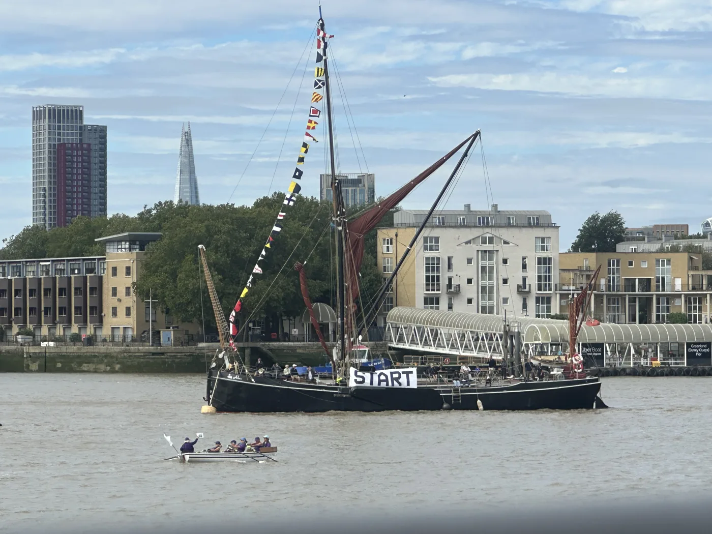 A rowing gig passes a sailing barge carrying a Start banner on the Thames
